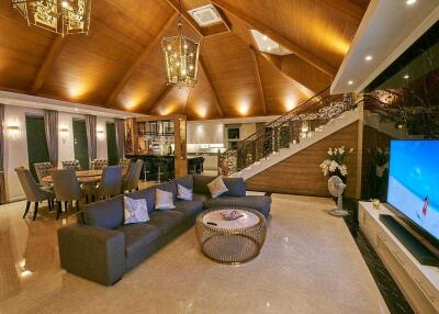 Spacious living room with high wooden ceiling, modern furniture, dining area, and staircase