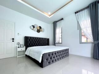 Bright modern bedroom with double bed, two windows with curtains, and wall art