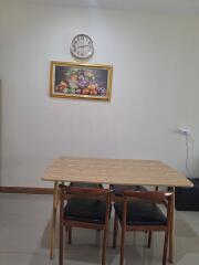 Dining area with wooden table, three chairs, wall clock, and fruit painting