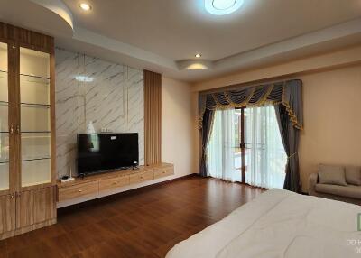 Spacious bedroom with a large TV, decorative shelving, wooden floor, and access to a balcony