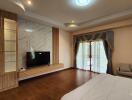 Spacious bedroom with a large TV, decorative shelving, wooden floor, and access to a balcony