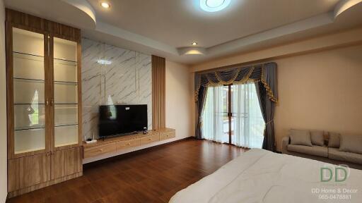 Spacious bedroom with a large TV, decorative shelving, wooden floor, and access to a balcony