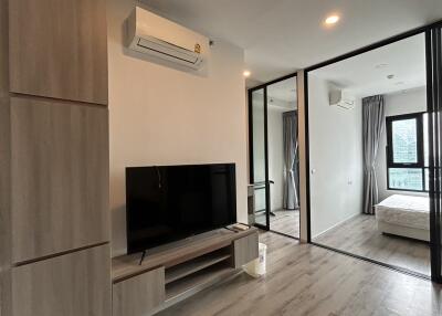 Modern living room featuring air conditioning, TV, and large window view into a bedroom