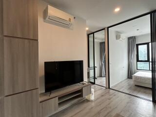 Modern living room featuring air conditioning, TV, and large window view into a bedroom