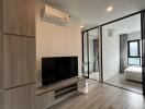 Modern living room featuring air conditioning, TV, and large window view into a bedroom