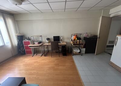 A small home office area within a living space featuring a desk, chairs, and various storage items.