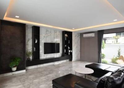 Modern living room with a marble accent wall, built-in black storage units, a flat-screen TV, a black sectional sofa, a small white coffee table, recessed lighting, and large windows with garden view.
