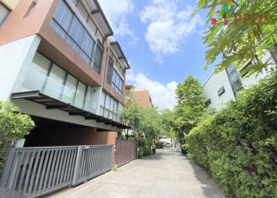 Modern multi-story building with large windows and a driveway lined with greenery on a sunny day