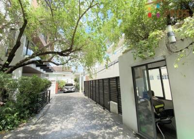 Exterior view of the property showing the driveway, greenery, and a small office or security room