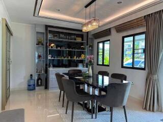 Modern dining room with glass table and six chairs, large windows, and built-in shelves