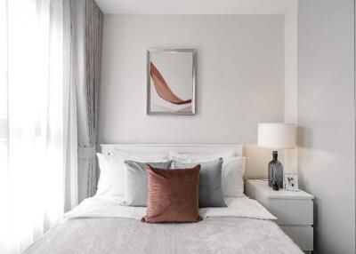 A modern bedroom with a neatly made bed, nightstand, lamp, and wall art