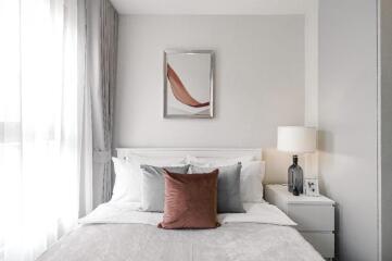 A modern bedroom with a neatly made bed, nightstand, lamp, and wall art