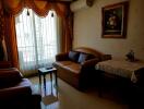 Living room with sofa, armchairs, coffee table, wall-mounted air conditioner, and large window with drapes