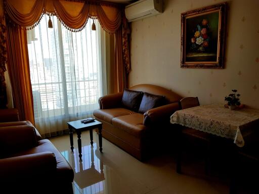 Living room with sofa, armchairs, coffee table, wall-mounted air conditioner, and large window with drapes