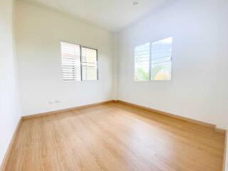 Spacious empty bedroom with wooden floors and two windows