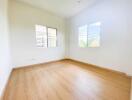 Spacious empty bedroom with wooden floors and two windows