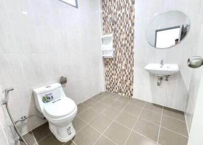 Modern bathroom with tiled walls and floor, equipped with toilet, sink, and mirror