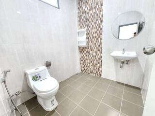 Modern bathroom with tiled walls and floor, equipped with toilet, sink, and mirror