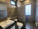 Modern bathroom with gray tiles, glass shower, and white fixtures