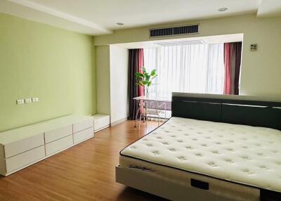 Spacious bedroom with green accent wall, queen-size bed, and a large window.