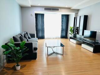 Modern living room with wooden flooring, sofa, coffee table, TV unit, and indoor plants