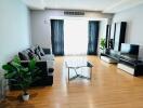 Modern living room with wooden flooring, sofa, coffee table, TV unit, and indoor plants