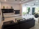 Modern living room with a black leather sofa, ceiling fans, and a glass coffee table