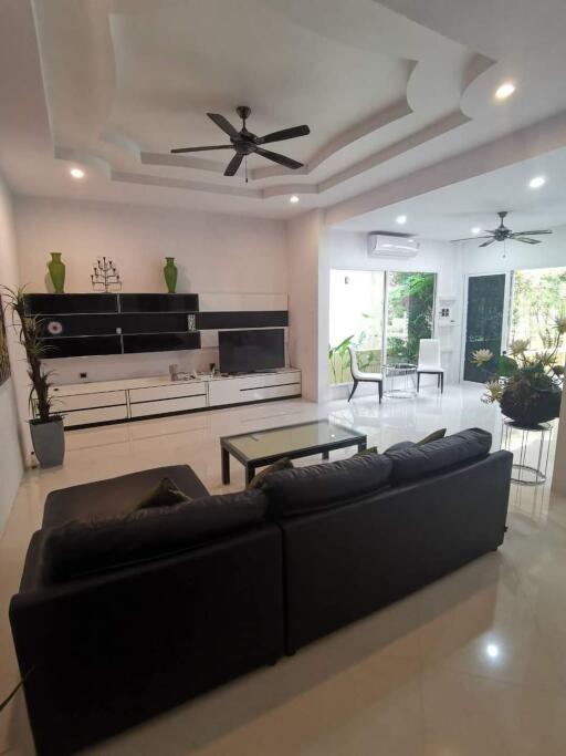 Modern living room with a black leather sofa, ceiling fans, and a glass coffee table