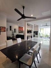 Modern dining room with black marble table, white cushioned chairs, and ceiling fan