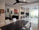 Modern dining room with black marble table, white cushioned chairs, and ceiling fan