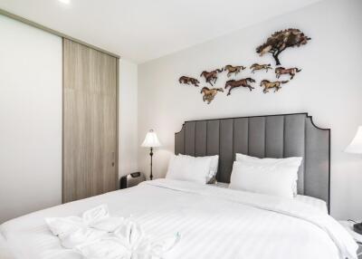 Modern bedroom with grey headboard, white bedding, two bedside lamps, and wall art featuring a tree and running horses