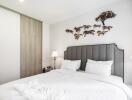 Modern bedroom with grey headboard, white bedding, two bedside lamps, and wall art featuring a tree and running horses