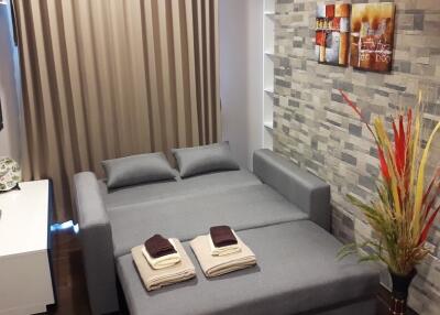 Modern bedroom with grey fold-out sofa bed, wall-mounted TV, and decorative accents