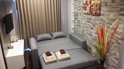 Modern bedroom with grey fold-out sofa bed, wall-mounted TV, and decorative accents