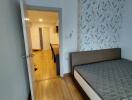 Bedroom with view into hallway featuring wooden flooring and patterned wallpaper