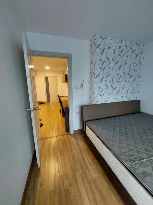 Bedroom with view into hallway featuring wooden flooring and patterned wallpaper