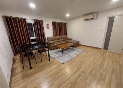 Modern living room with wooden flooring, brown leather sofa, dining table, and air conditioning