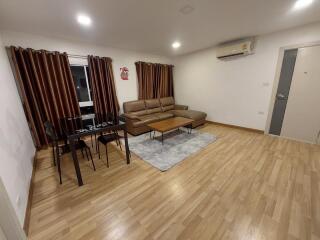 Modern living room with wooden flooring, brown leather sofa, dining table, and air conditioning