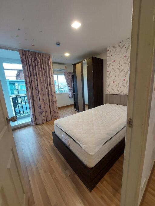 A cozy bedroom with wooden flooring, a large bed, wardrobe, window with curtains, and a balcony view.