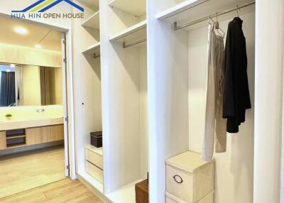 Walk-in closet with white shelves and hanging clothes, leading to a modern bathroom