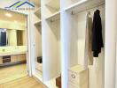 Walk-in closet with white shelves and hanging clothes, leading to a modern bathroom