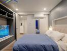 Modern bedroom with blue bedding, wall-mounted TV, and storage units