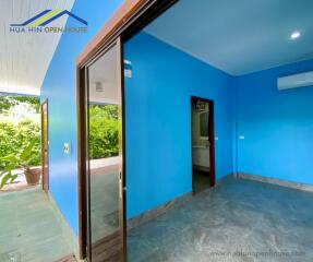 A bright bedroom with blue walls and tiled flooring, featuring an air conditioner and attached bathroom.