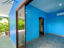 A bright bedroom with blue walls and tiled flooring, featuring an air conditioner and attached bathroom.