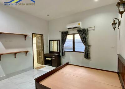 Spacious furnished bedroom with wooden bedframe and vanity, with adjacent bathroom