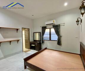 Spacious furnished bedroom with wooden bedframe and vanity, with adjacent bathroom