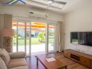 Bright living room with large windows, a ceiling fan, a wall-mounted TV, and wooden furniture