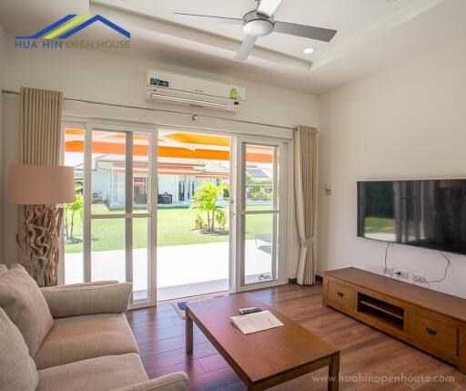 Bright living room with large windows, a ceiling fan, a wall-mounted TV, and wooden furniture