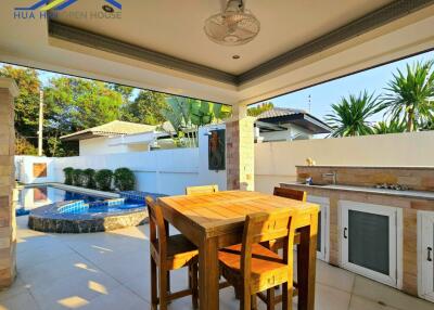 Outdoor dining area with wooden table and chairs, adjacent to swimming pool and kitchen counter