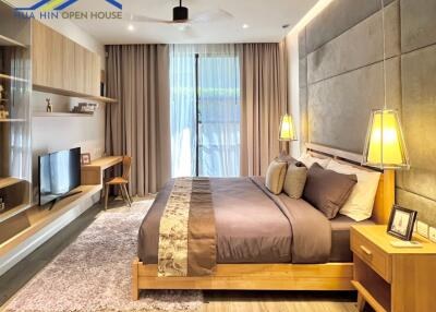Modern bedroom with a queen-sized bed, bedside tables with lamps, a wall-mounted TV, and a sliding glass door.